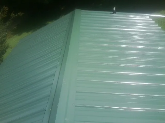 New green metal panels meeting at the ridge of a roof — Flat Roof Repair work by our crew in Galesburg