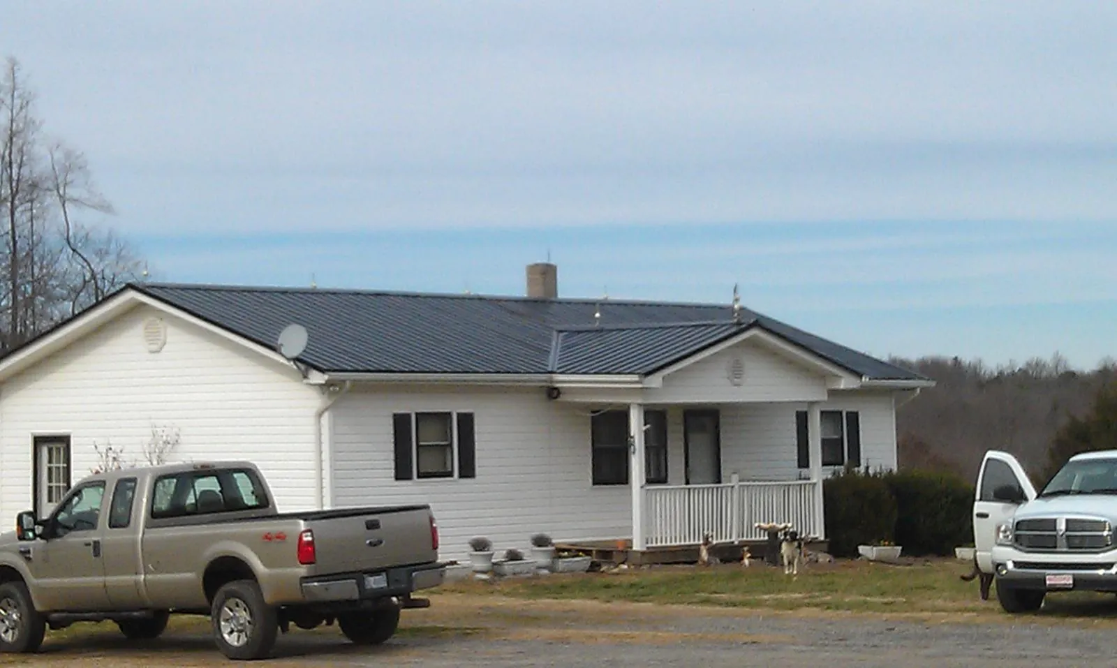 Finished dark metal roof on a white ranch home with work trucks parked in Galesburg